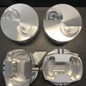 Top view of four aluminum pistons on a dark work surface: two complete pistons above, two cutaway pistons below showing inner chambers.